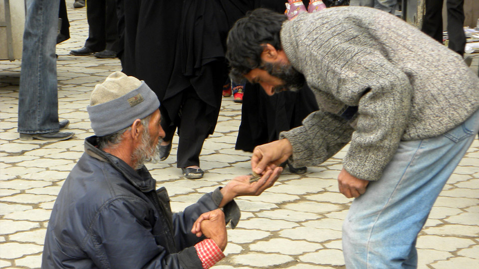  A man is giving money to a beggar on the street with the intention of paying zakat penghasilan, which is an obligatory annual payment made by Muslims to help those in need.